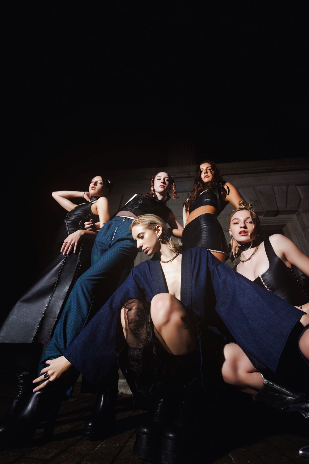 A dynamic group pose in dark blue outfits and boots against a black background with dramatic lighting and poses.