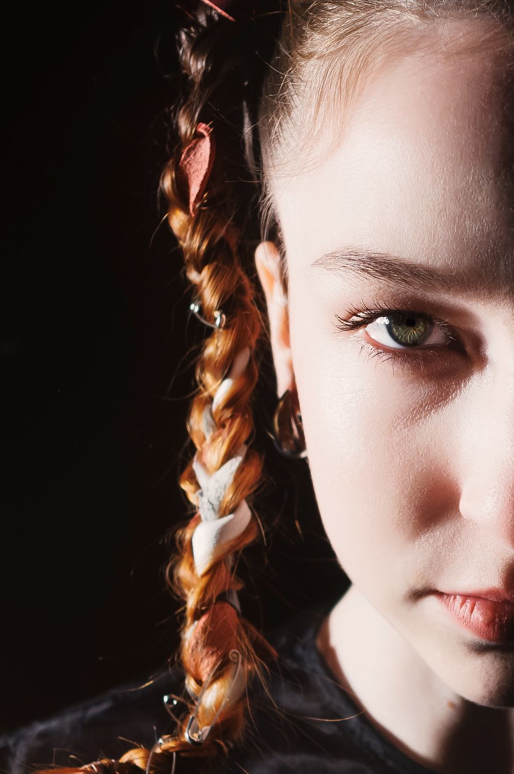 An artistic split portrait showing half of a face against dark background with illumination on auburn braided hair.