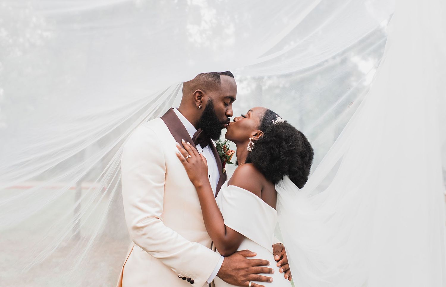 Bride and groom sharing a romantic kiss under a flowing white veil on their wedding day.