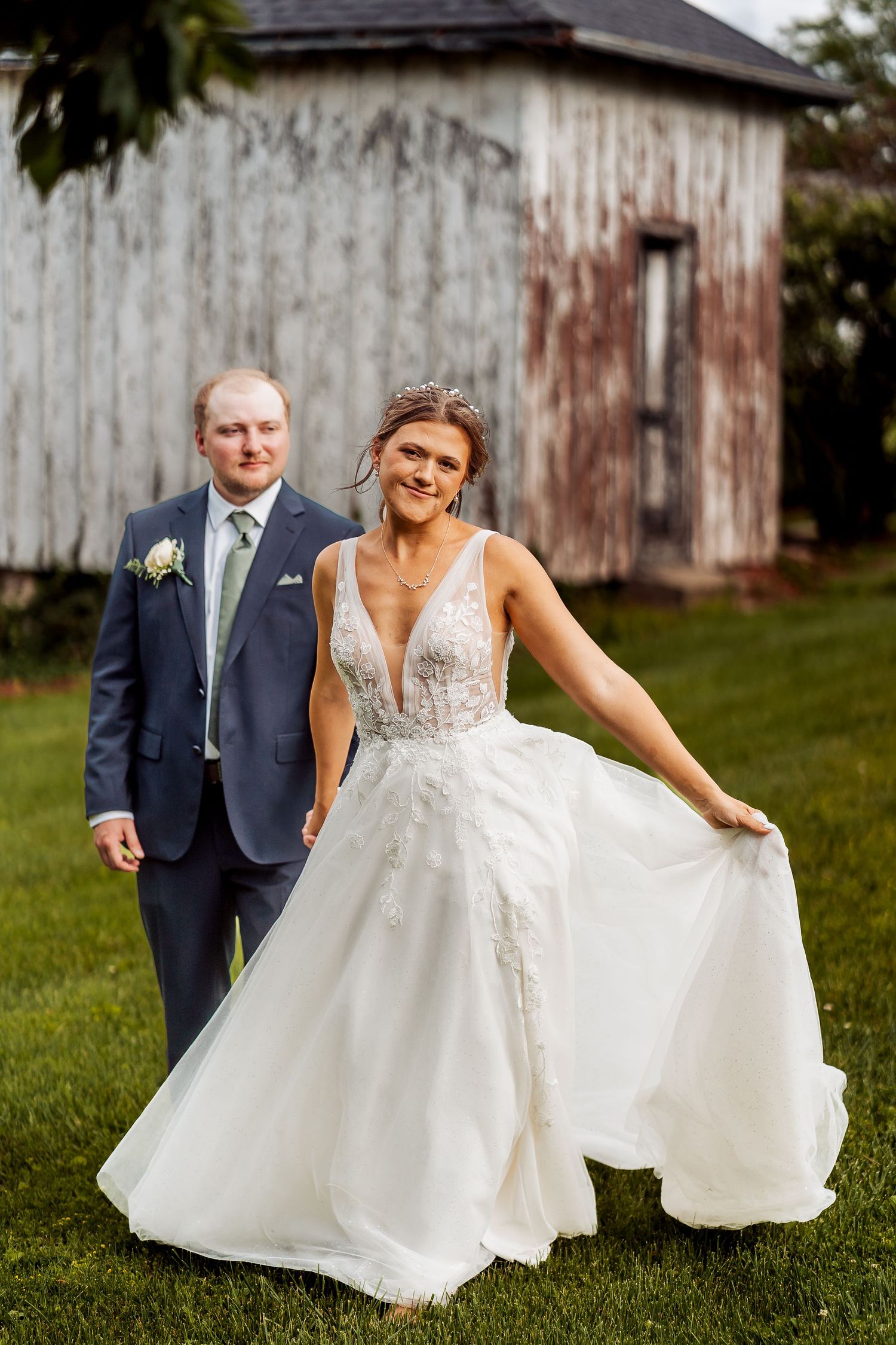 A couple poses for wedding photos in front of a rustic barn, with the bride showing off her flowing white dress.