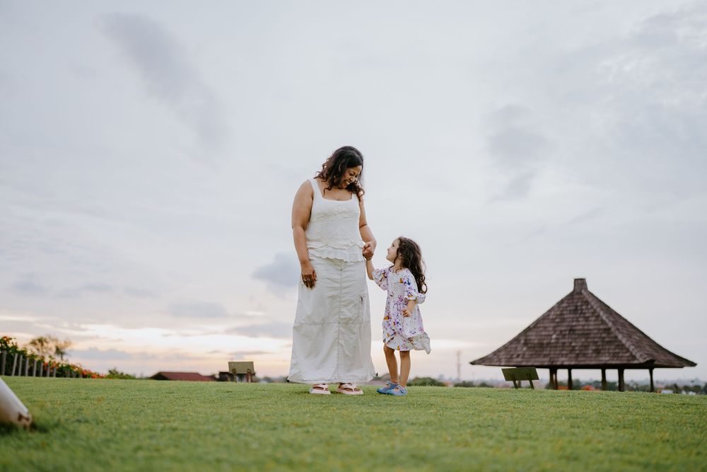 A tender moment shared between two people on grassy hill with traditional thatched hut in background.