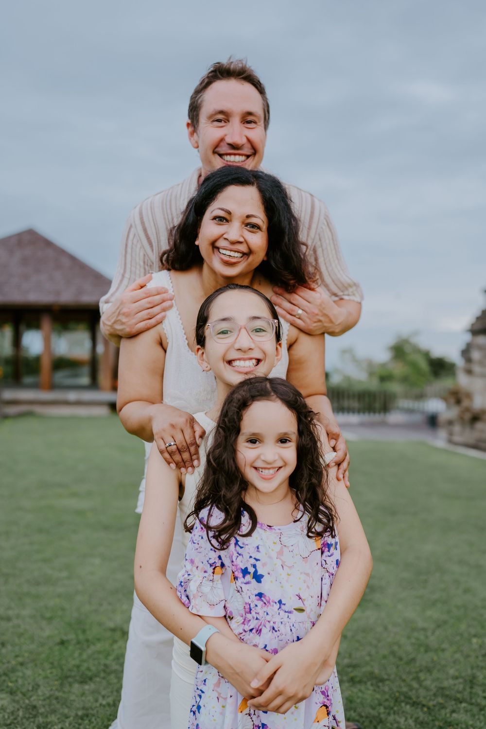 A joyful family plays together on a grassy lawn with a cloudy sky in the background.