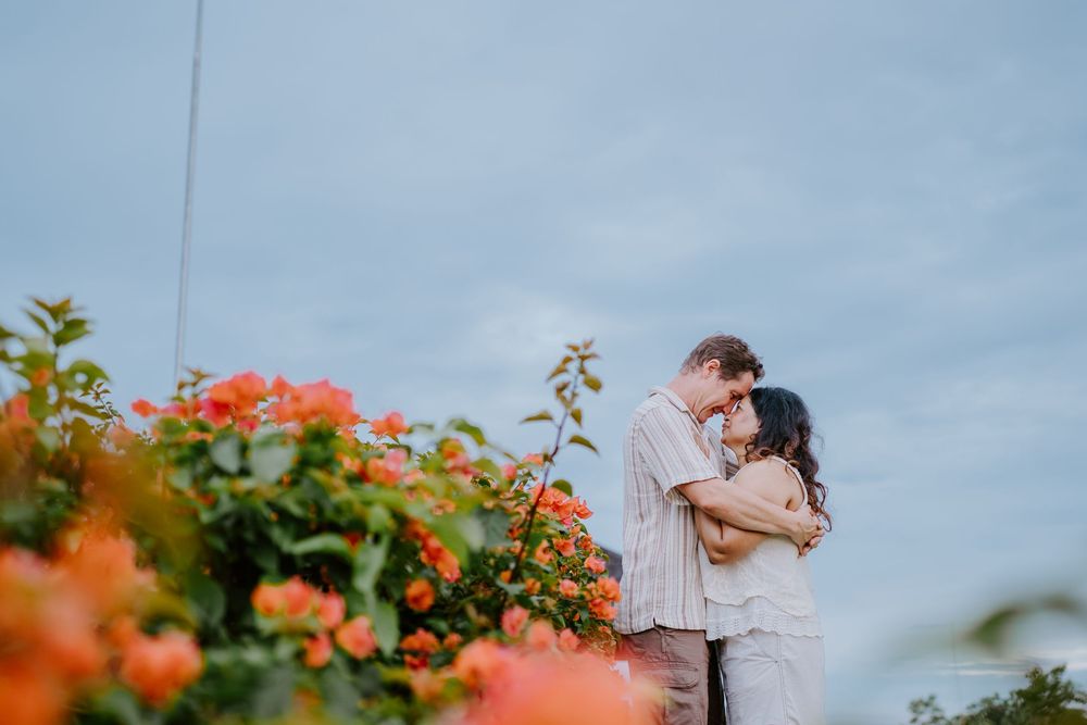 A romantic embrace among orange flowers with cloudy sky backdrop in tropical setting.