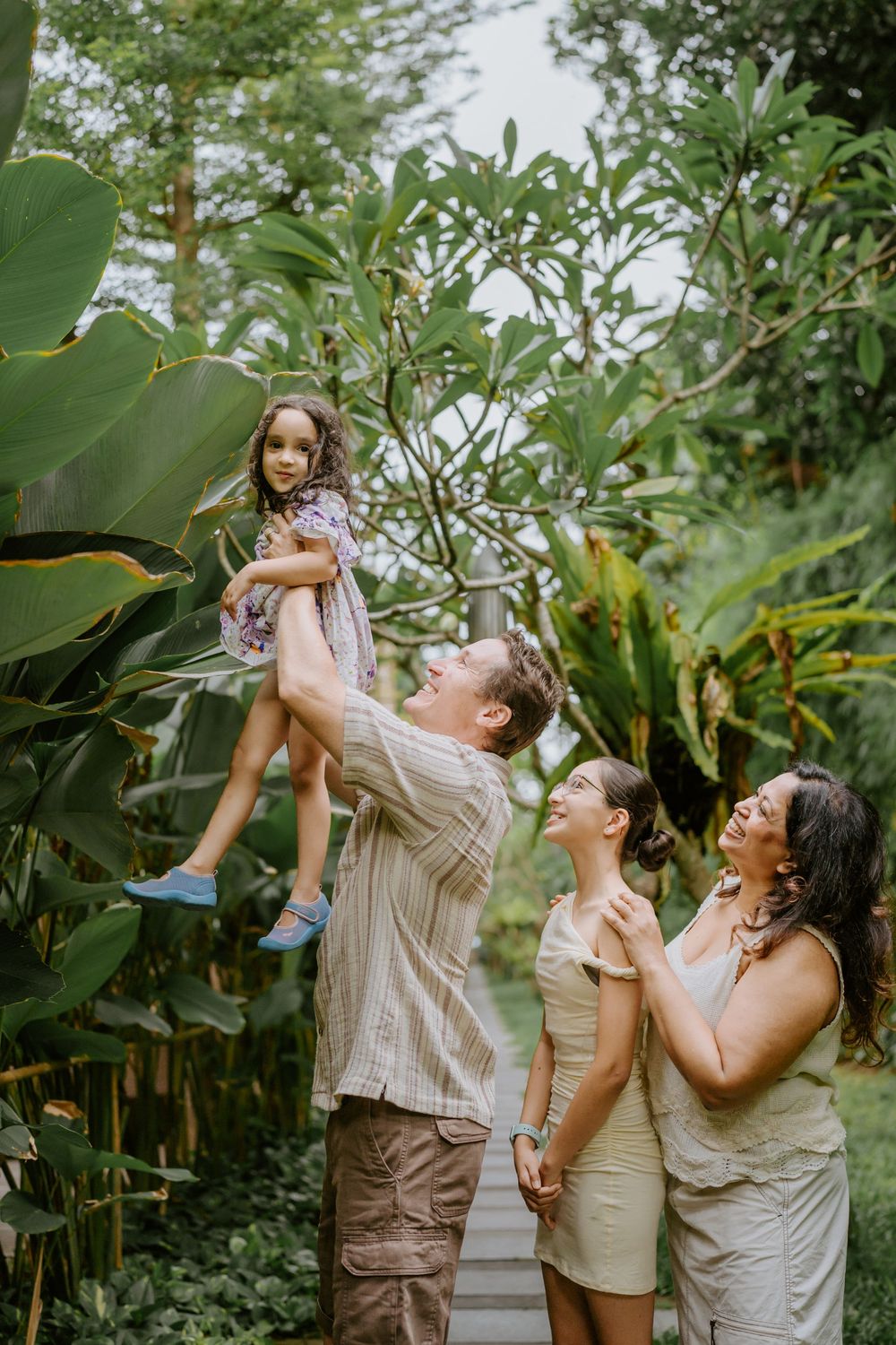 A family plays and laughs together surrounded by large tropical plants and greenery.