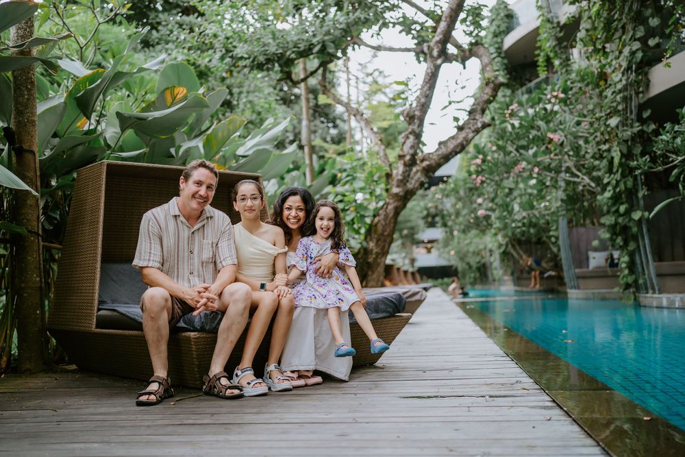 A family walks along a wooden boardwalk surrounded by tropical landscaping.