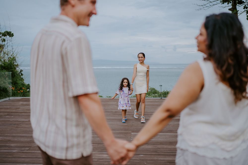 A family walks together on a wooden deck overlooking the ocean.
