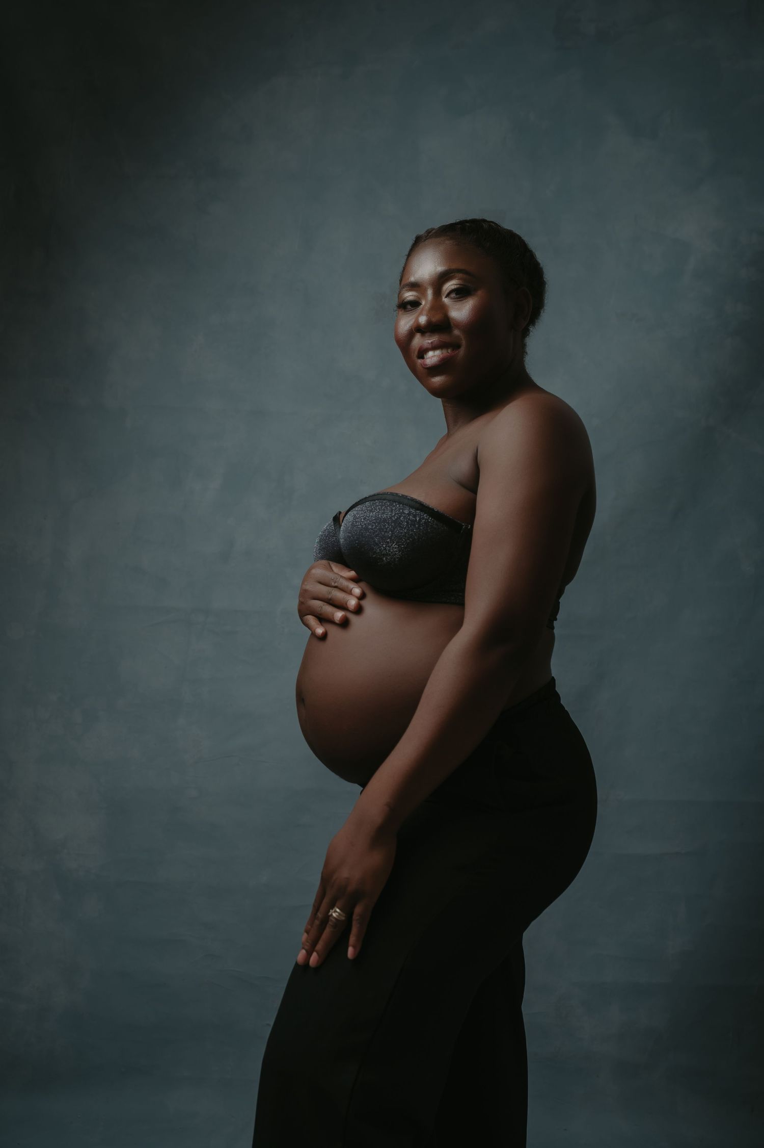 Artistic maternity photo showing a pregnant silhouette draped in flowing white fabric against a moody dark background.