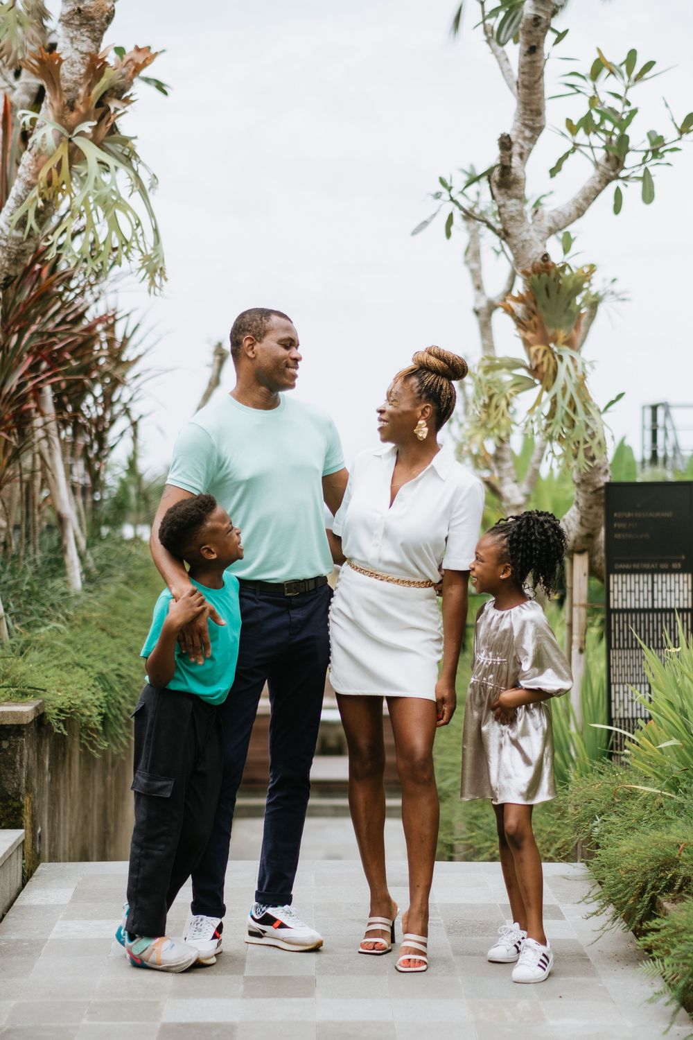 A family poses together on a walkway surrounded by tropical plants and trees.