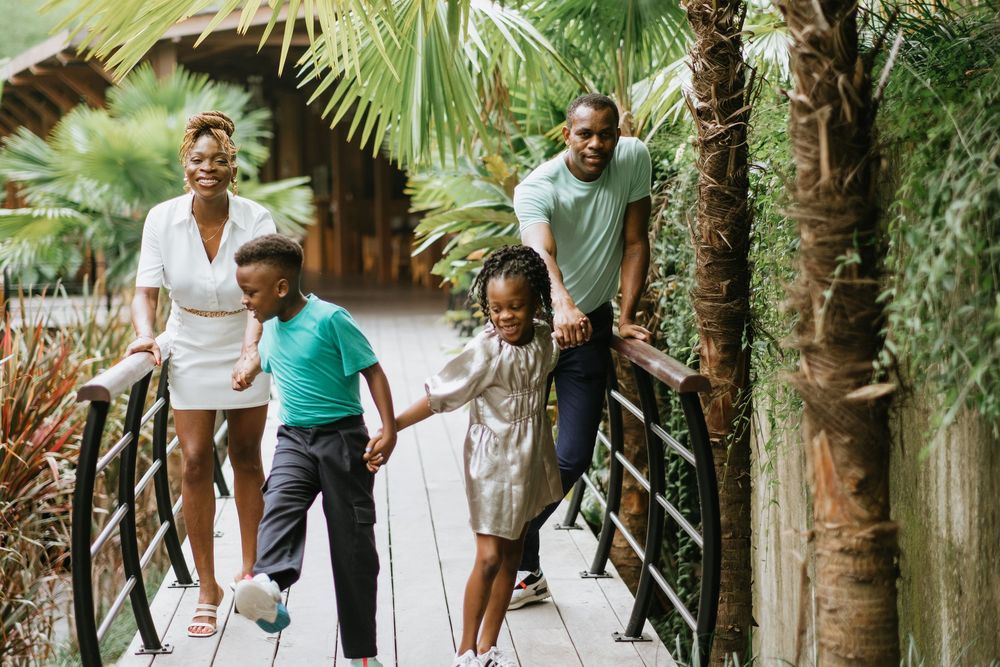A family walks together along a wooden bridge pathway surrounded by palm trees.