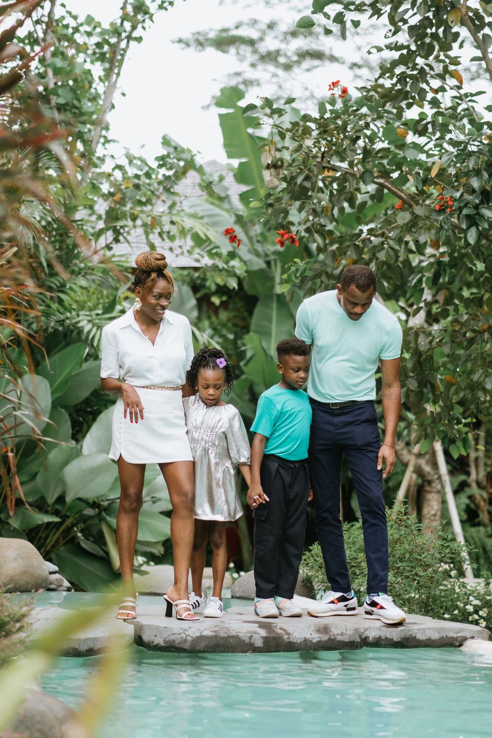 A family stands together on stone steps overlooking a tropical pool.