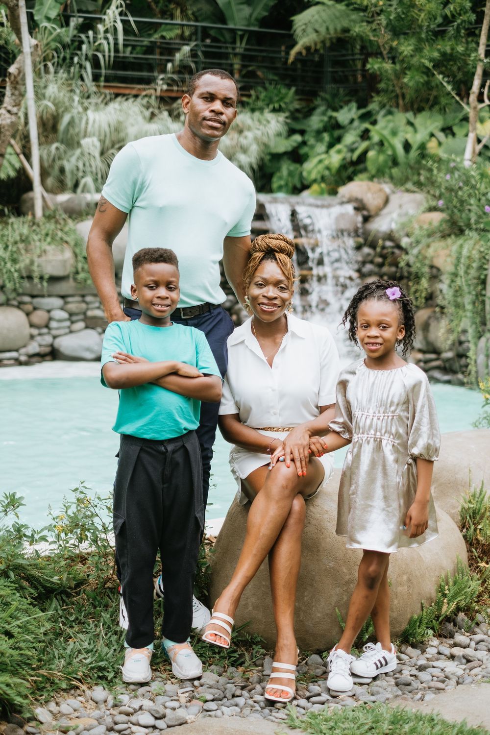 A family of four poses together near a waterfall and pool in a tropical garden.