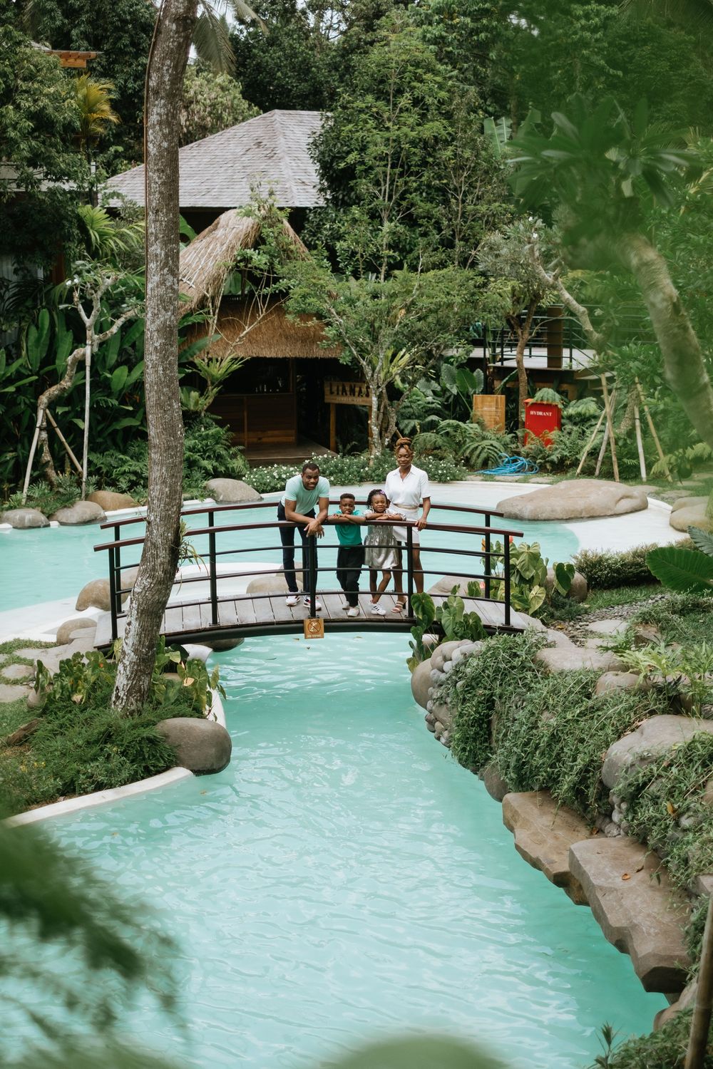 Turquoise pool with wooden bridges and lush greenery in a tropical resort setting.