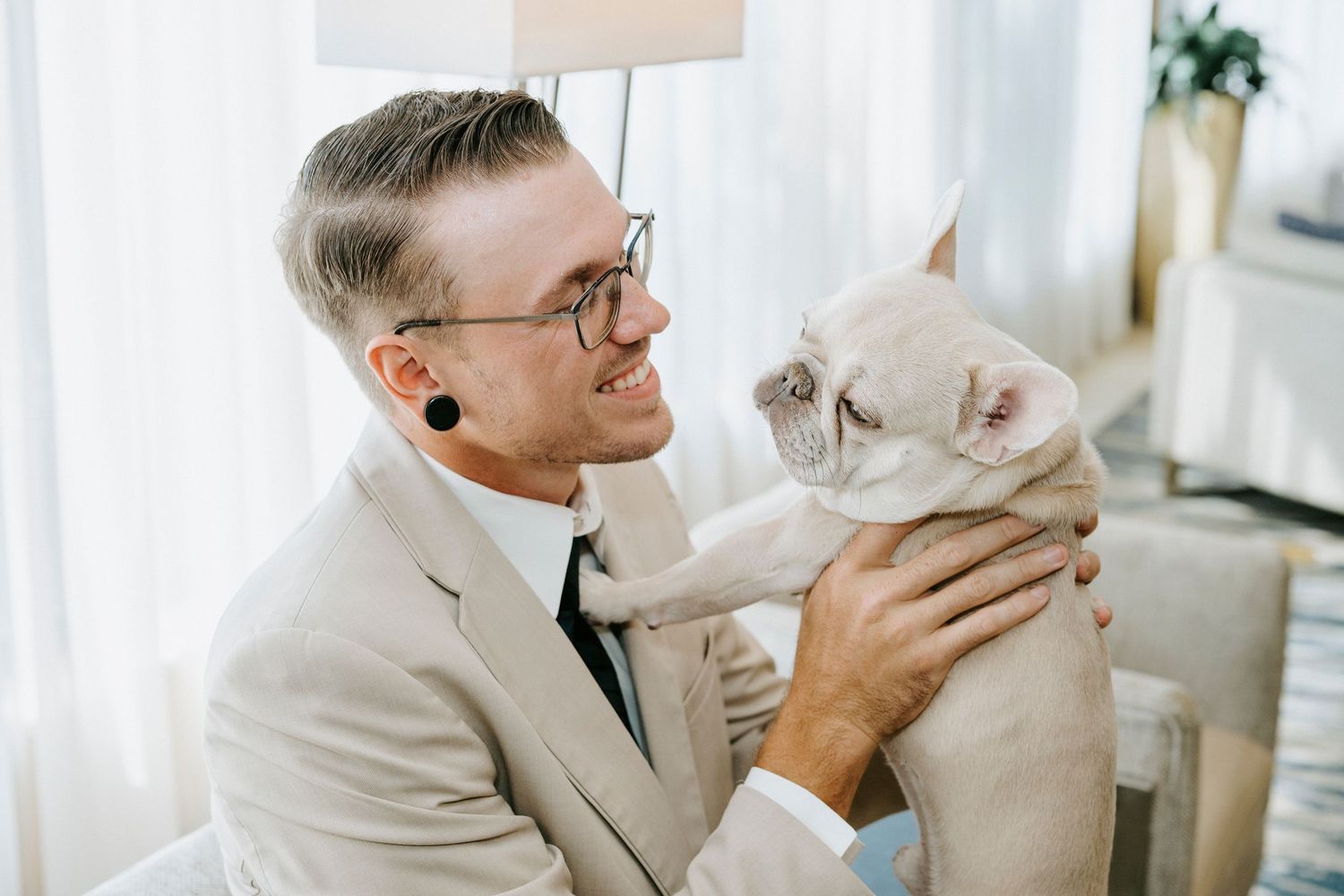 A tender moment between a person in off-white attire and a fluffy white cat by a bright window.