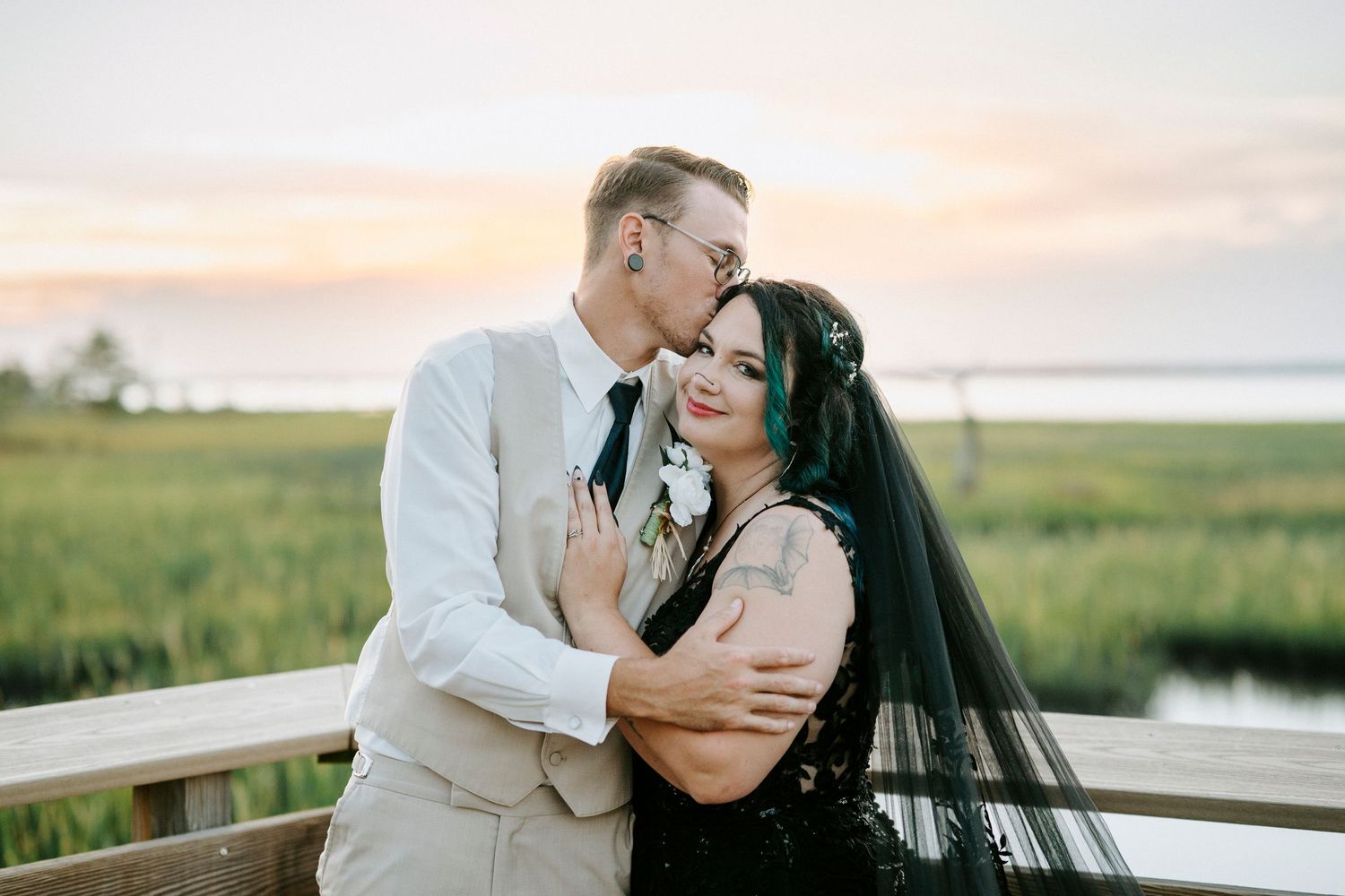 A couple shares a romantic embrace against a scenic marsh landscape at sunset.