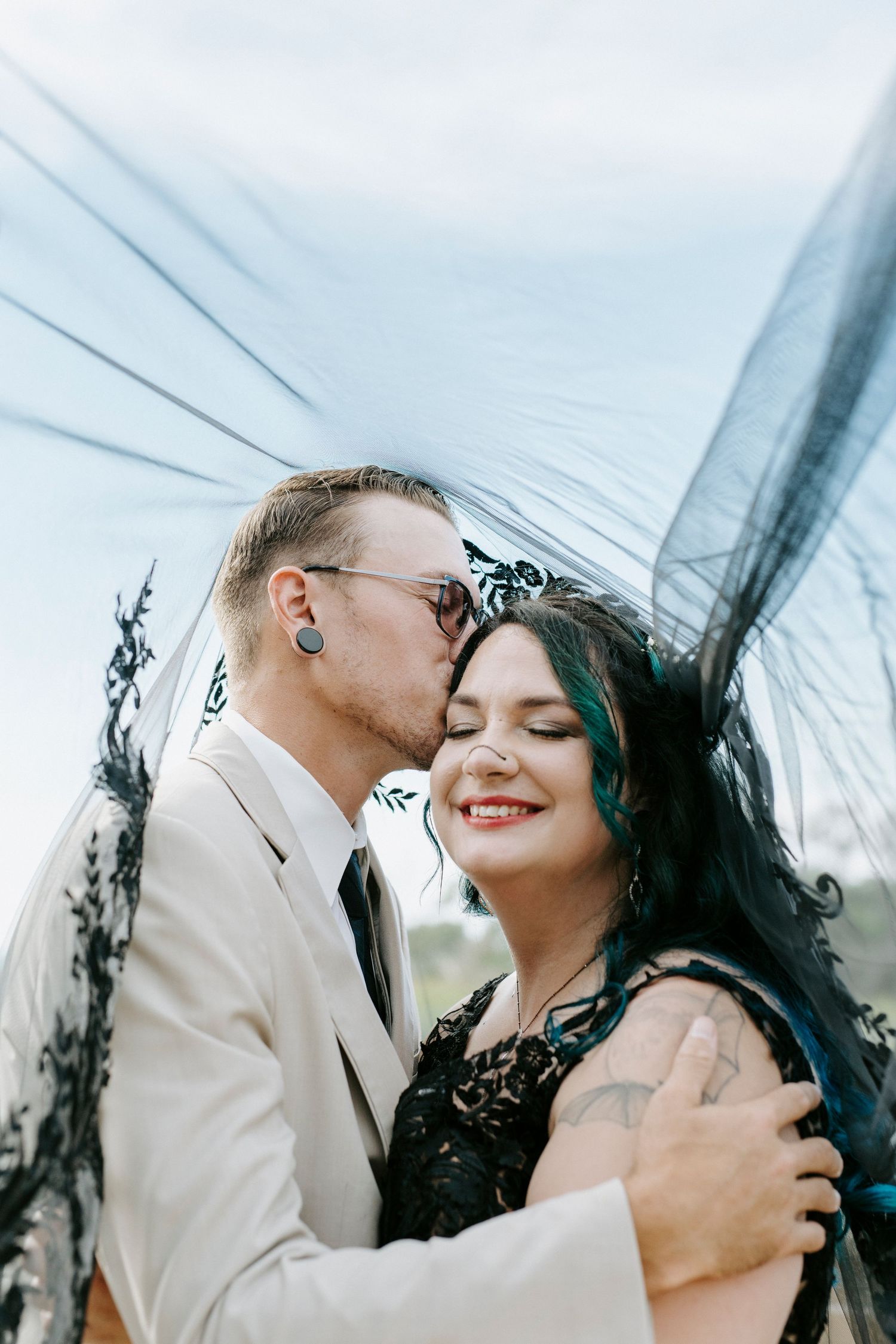 A tender moment between newlyweds with a black veil flowing in the breeze.
