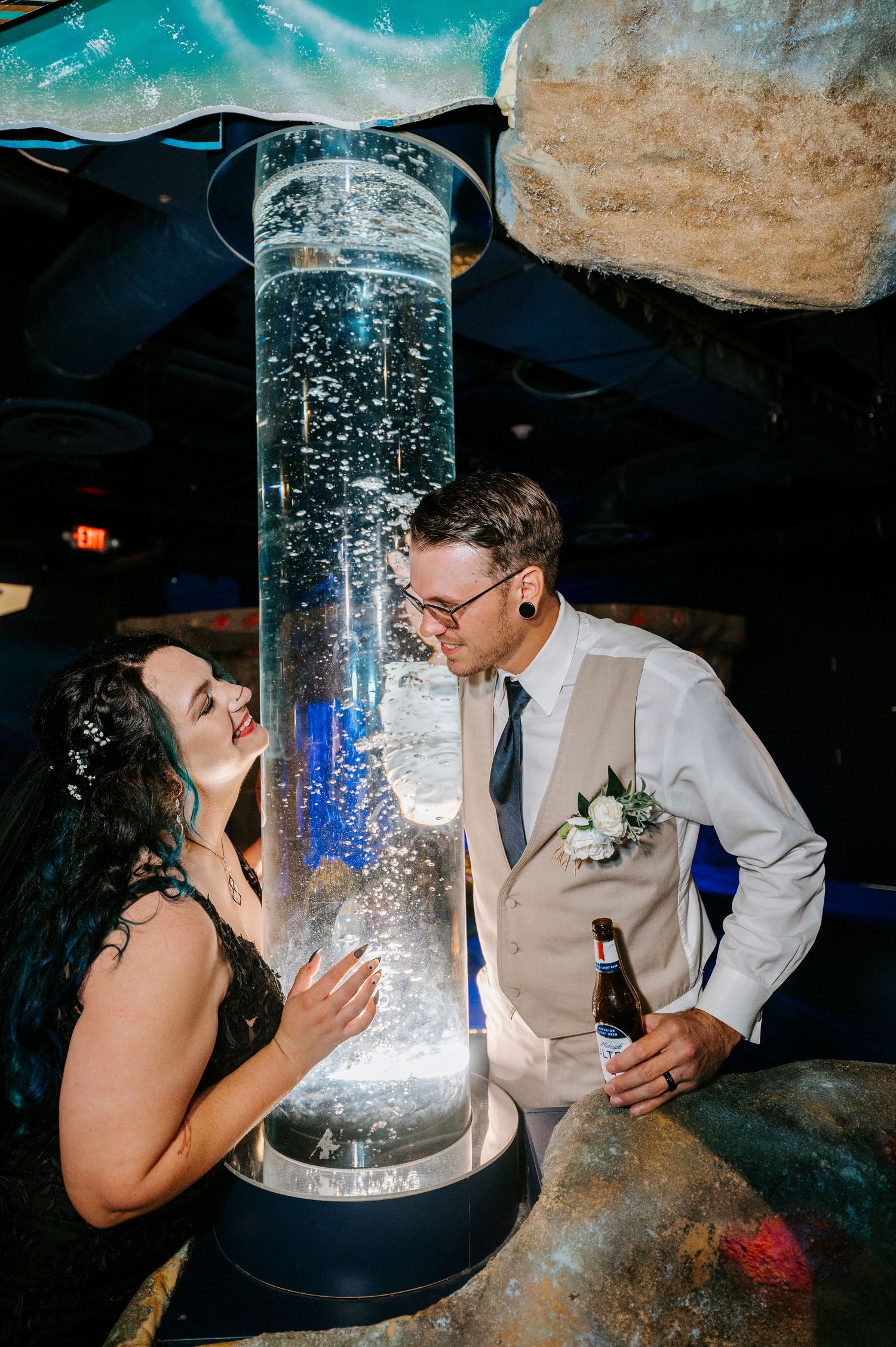 A couple drinks from a glass cylinder filled with bubbling liquid at a dimly lit venue.