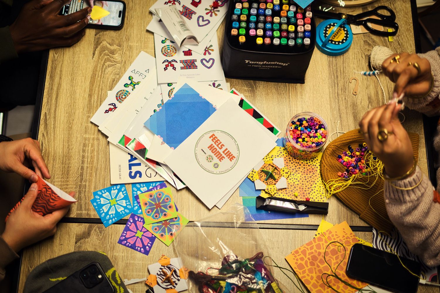 Crafting supplies including scissors, markers, stickers and paper scattered on a wooden table during a creative project.
