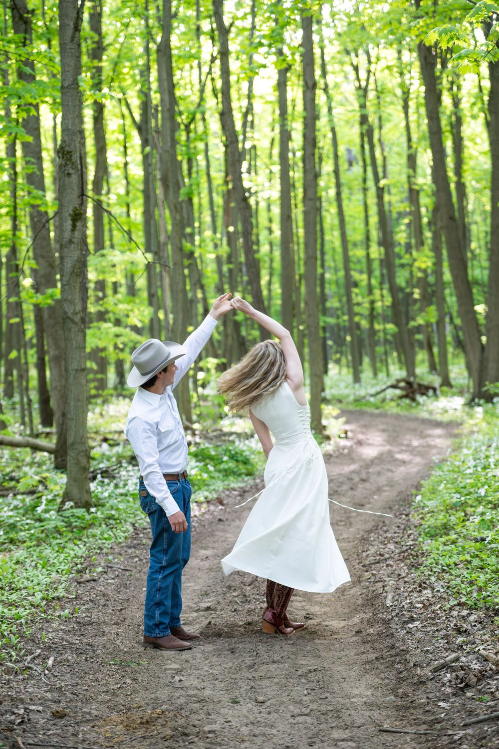 A couple dancing and twirling in a lush green forest setting during a romantic outdoor photo session.