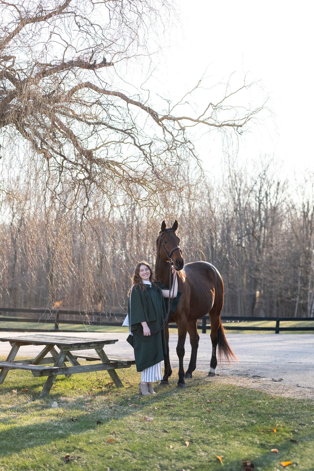 Person and horse enjoying a peaceful moment together in an outdoor paddock with bare winter trees in the background.