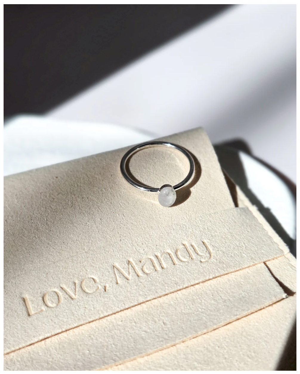 Close-up of a silver ring atop an embossed 'Love, Mandy' text on cream-colored paper in elegant lighting.