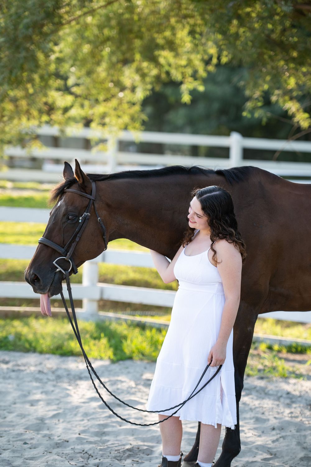 A woman in white clothing hugs and kisses a dark brown horse in a fenced riding arena.