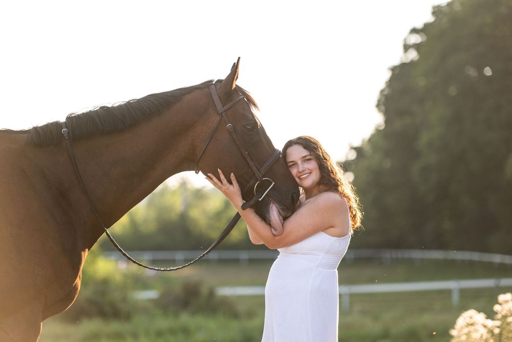 Someone wearing a white dress poses while holding a recurve bow and arrow at golden hour.