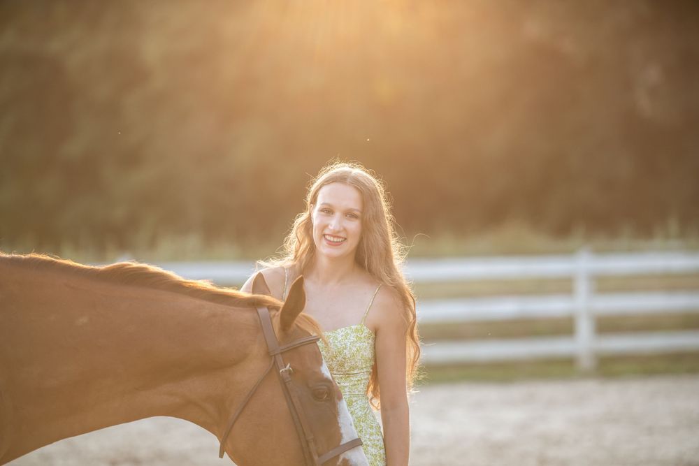 A woman in floral dress walks along a white fence at sunset during a golden hour photoshoot.