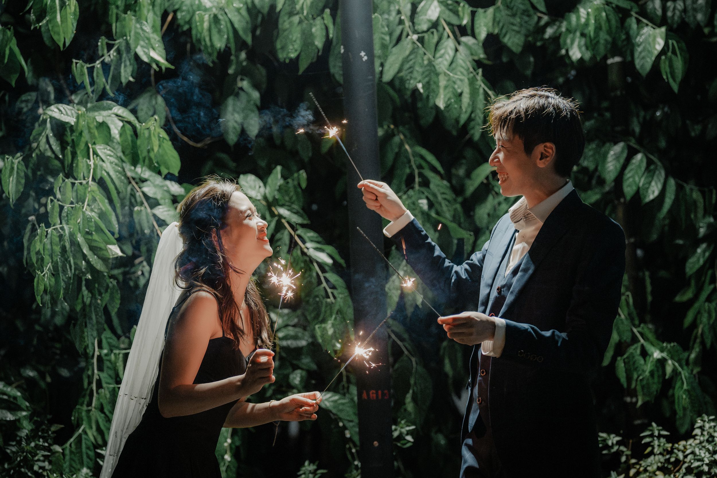 Wedding couple playing with sparklers against lush green foliage backdrop.