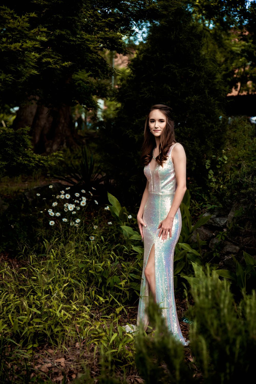 Young woman wearing a silver dress poses among the trees before prom