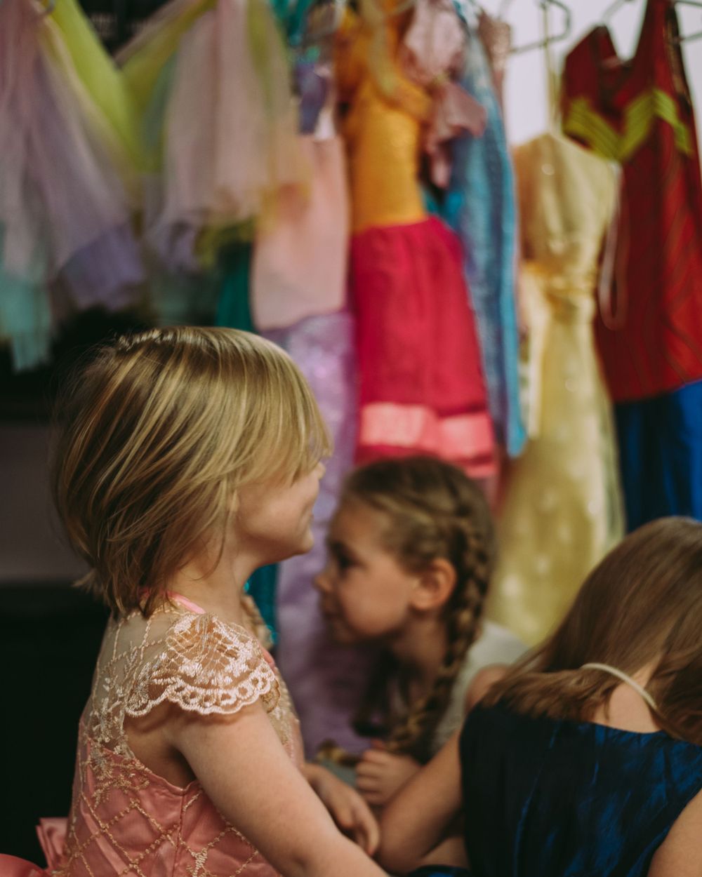 Little girls at Princess Birthday Party run around in front of a line of princess dresses