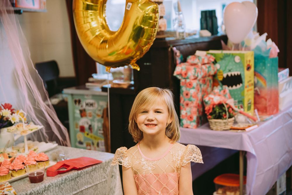 Birthday girl standing in front of her gifts and cake in a princess dress