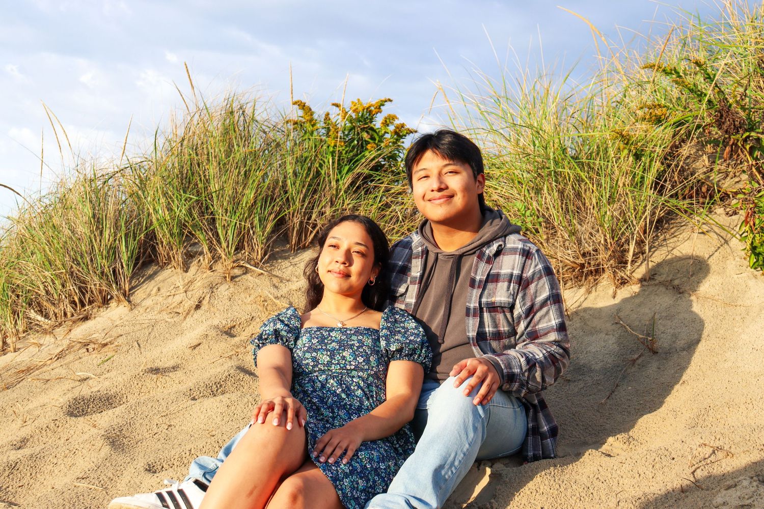 Couple sitting together on sandy dune with beach grass in background.