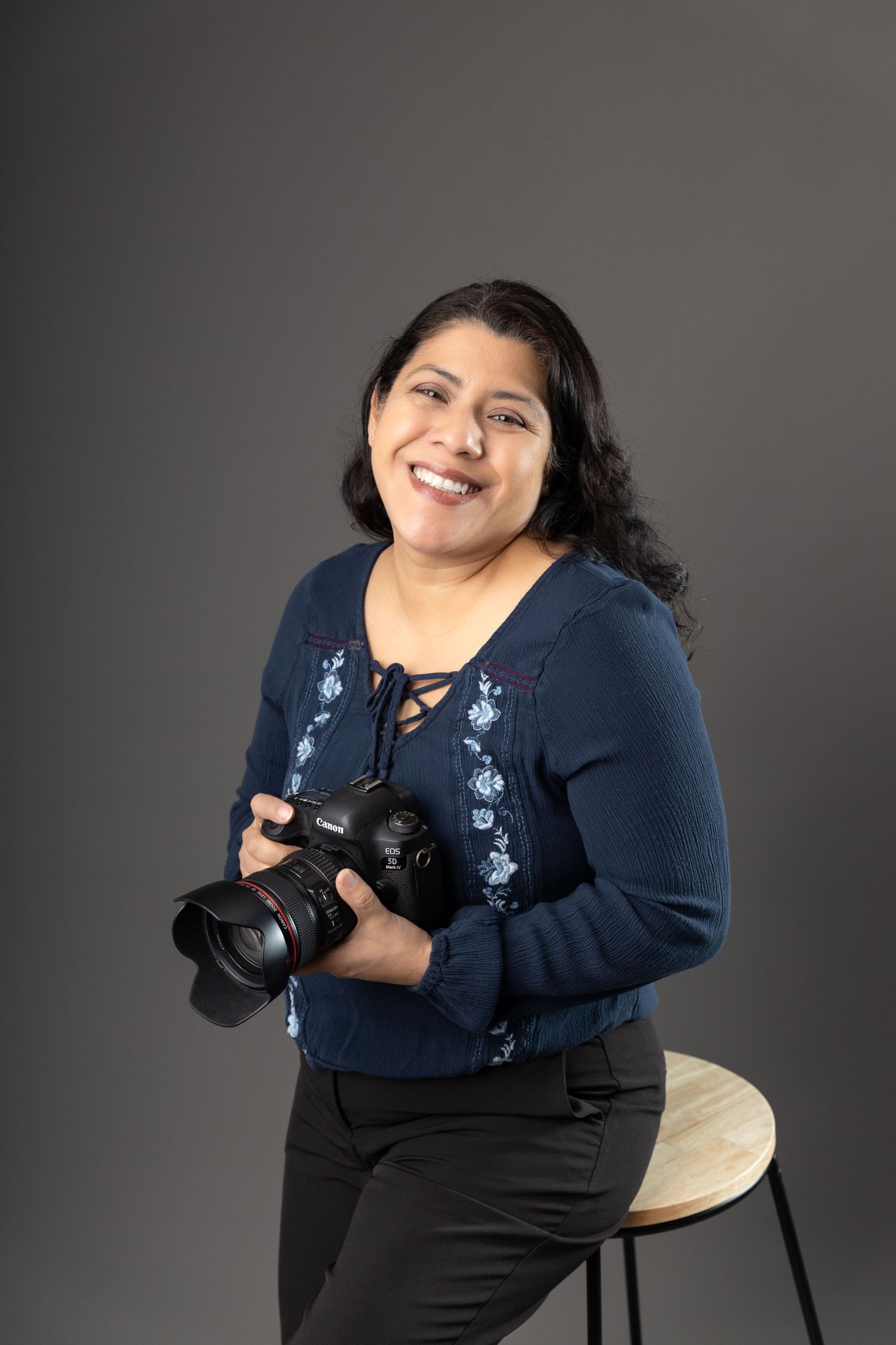 Photographer in casual attire poses with camera on brown studio backdrop.