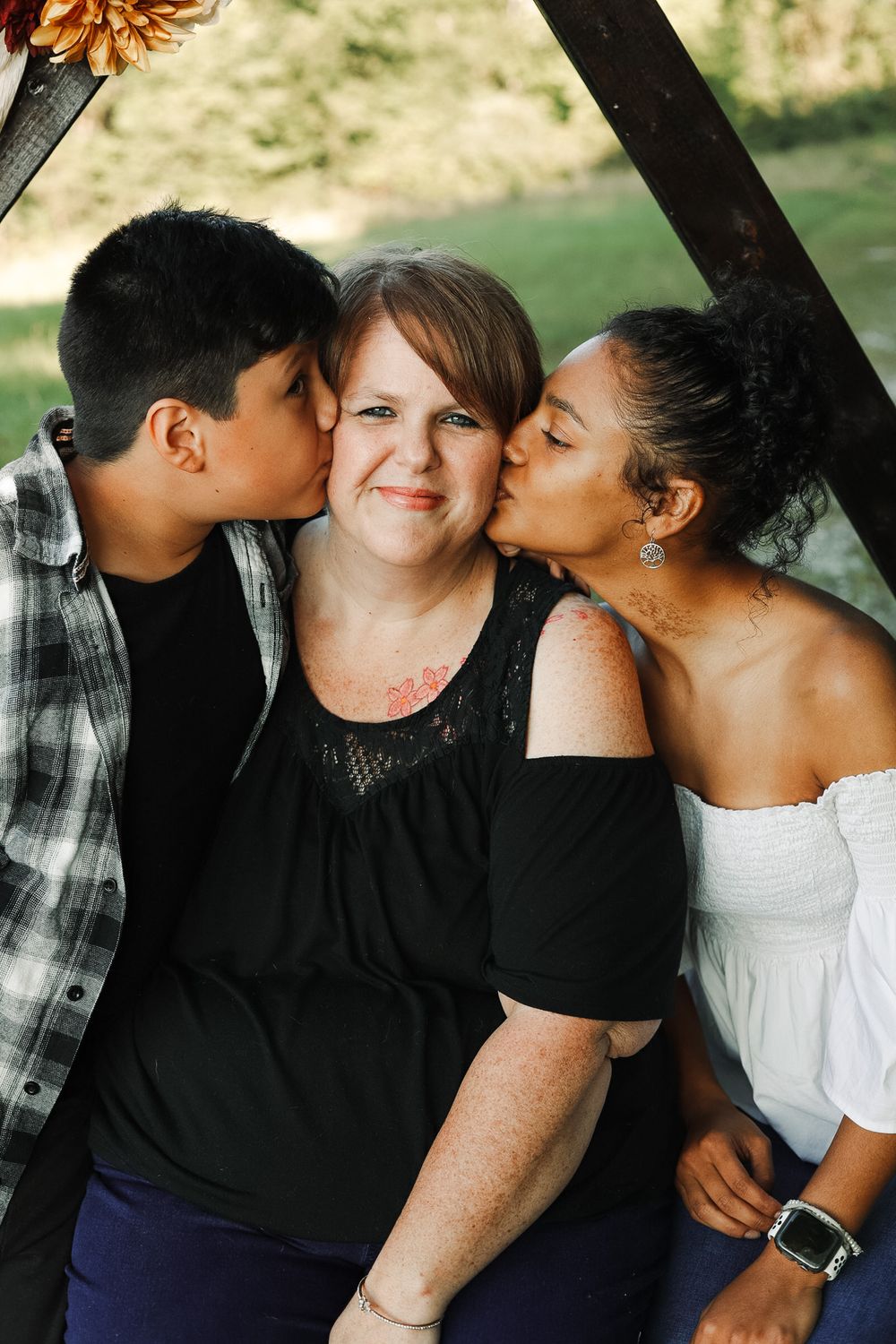 Friends sharing affectionate moments during outdoor photo session under wooden frame.