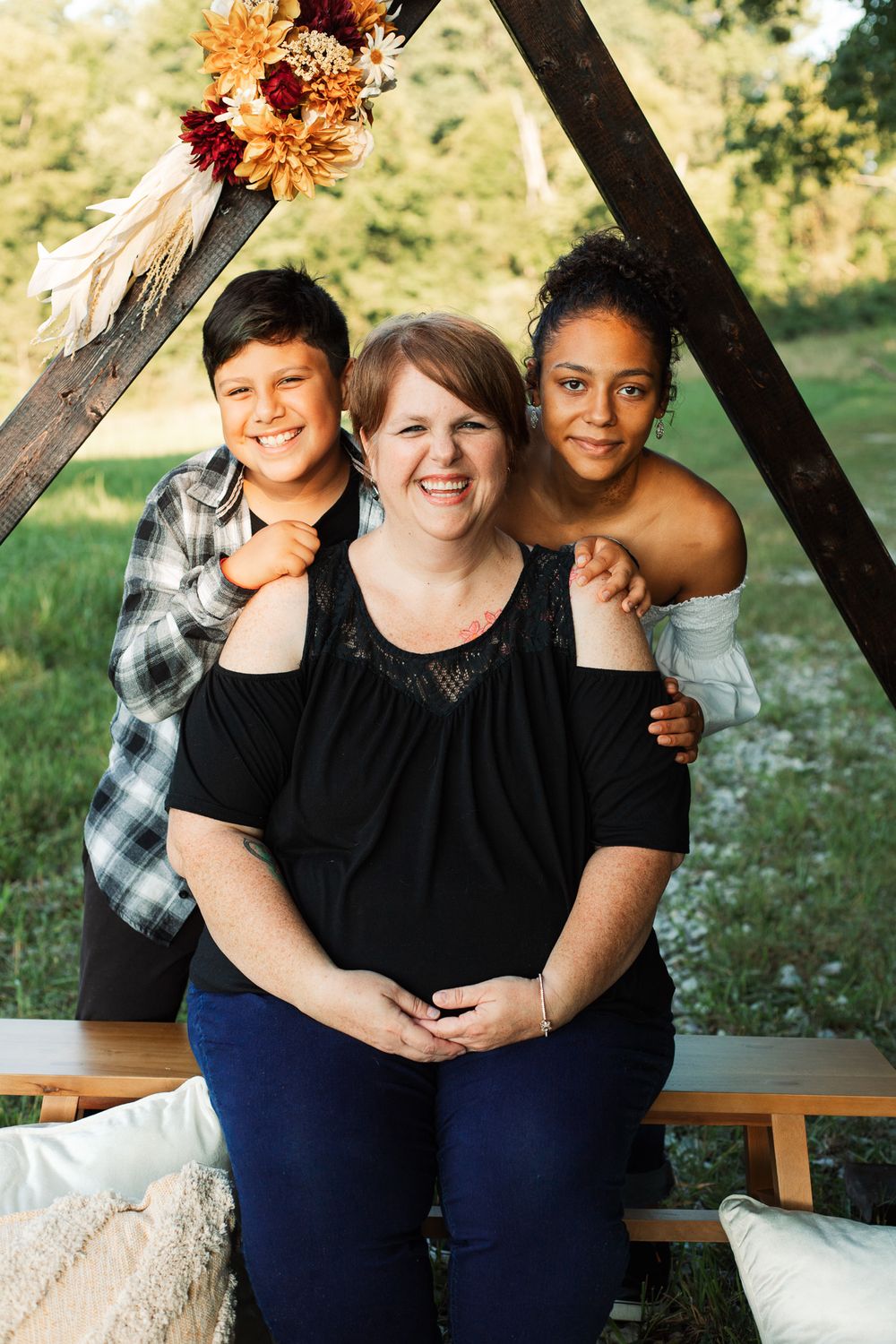 Three friends share joyful moments on a wooden bench decorated with autumn flowers.