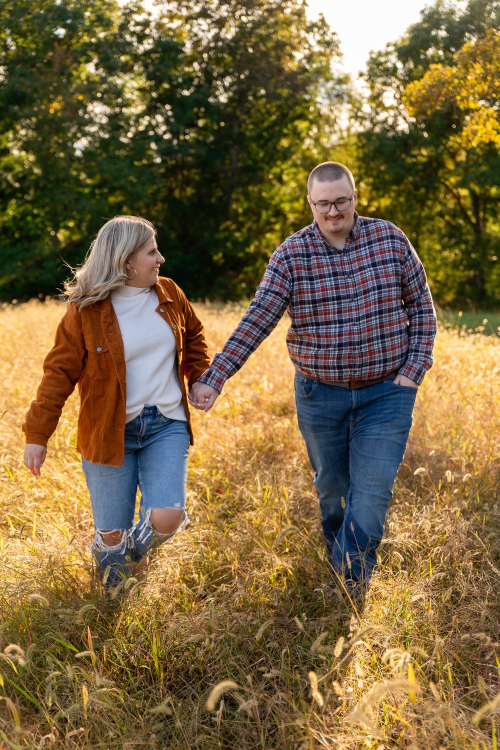 Couple walking hand in hand through tall golden grass during sunset in a field.