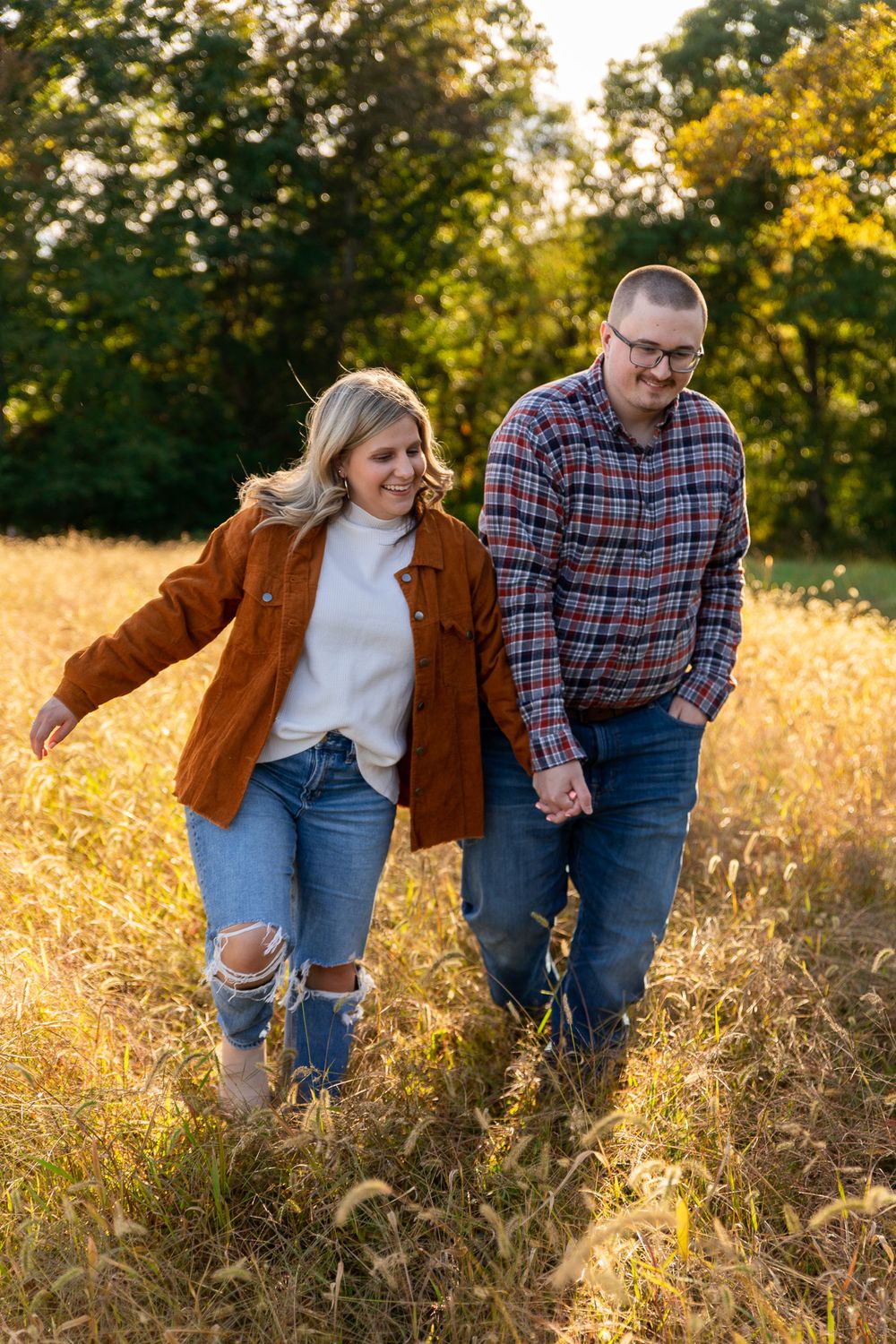 Couple walking through tall grass in autumn sunlight wearing casual denim and plaid.