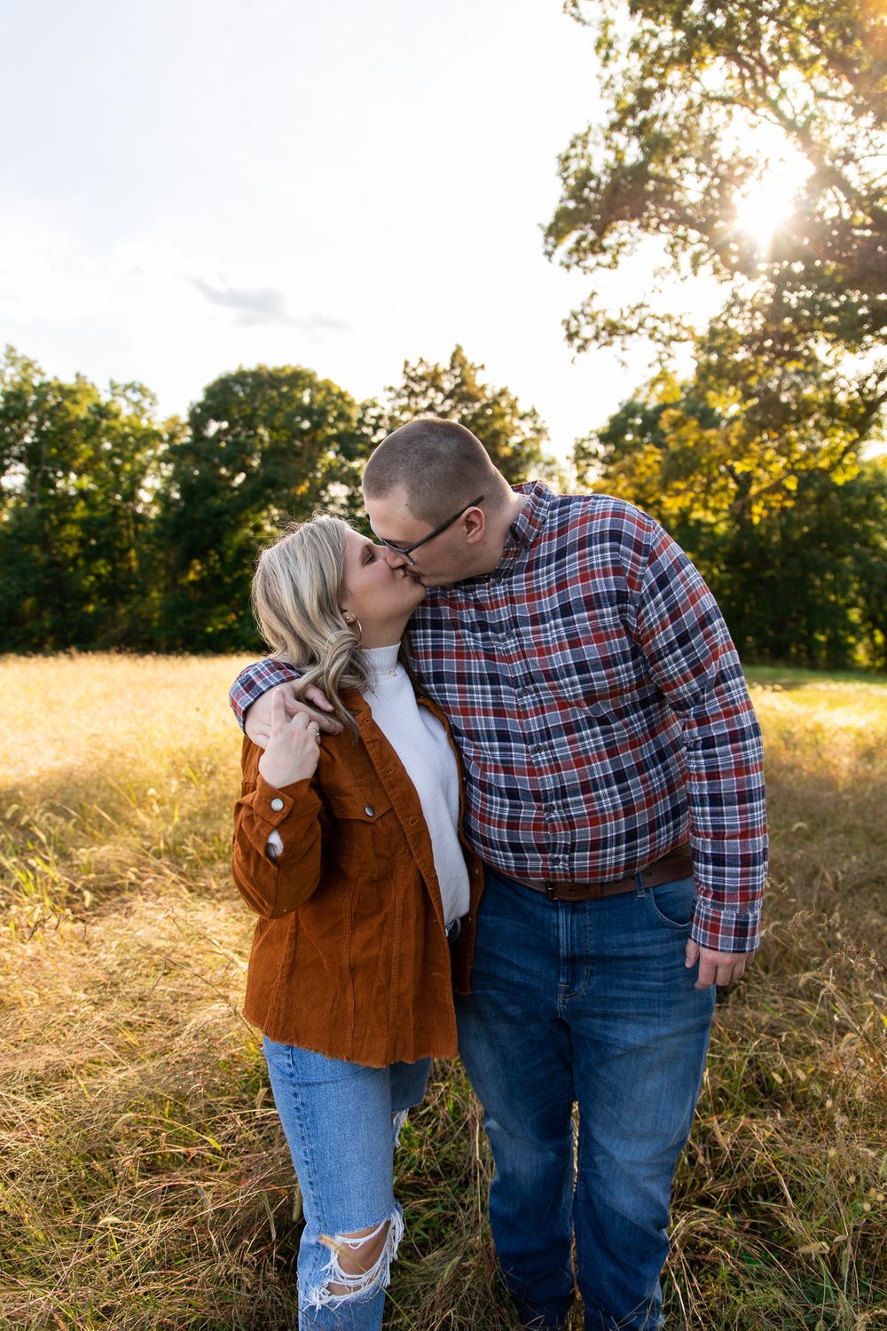 Romantic couple embracing in golden field during sunset photoshoot.