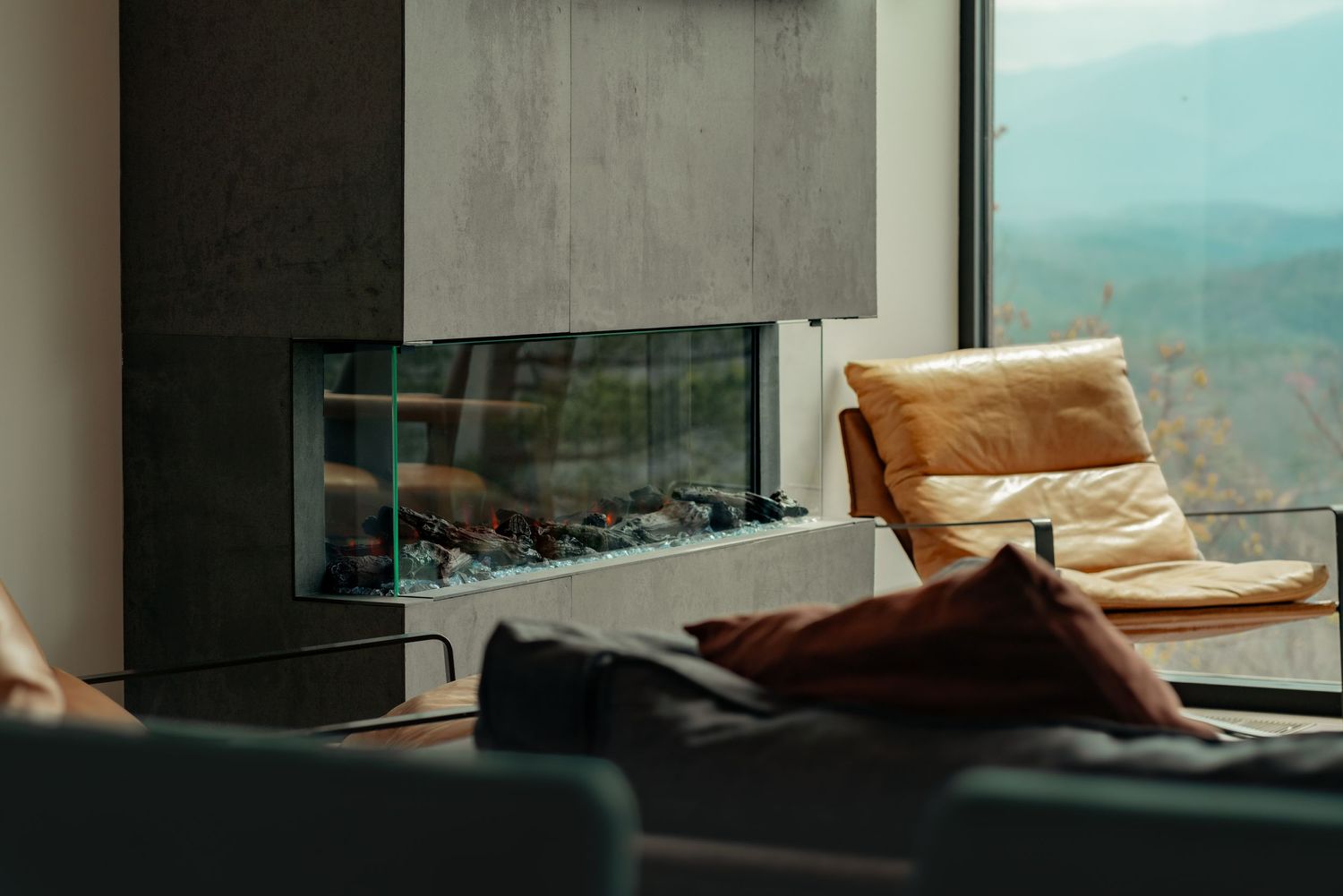 Modern living room interior with fireplace and mountain view through large windows.