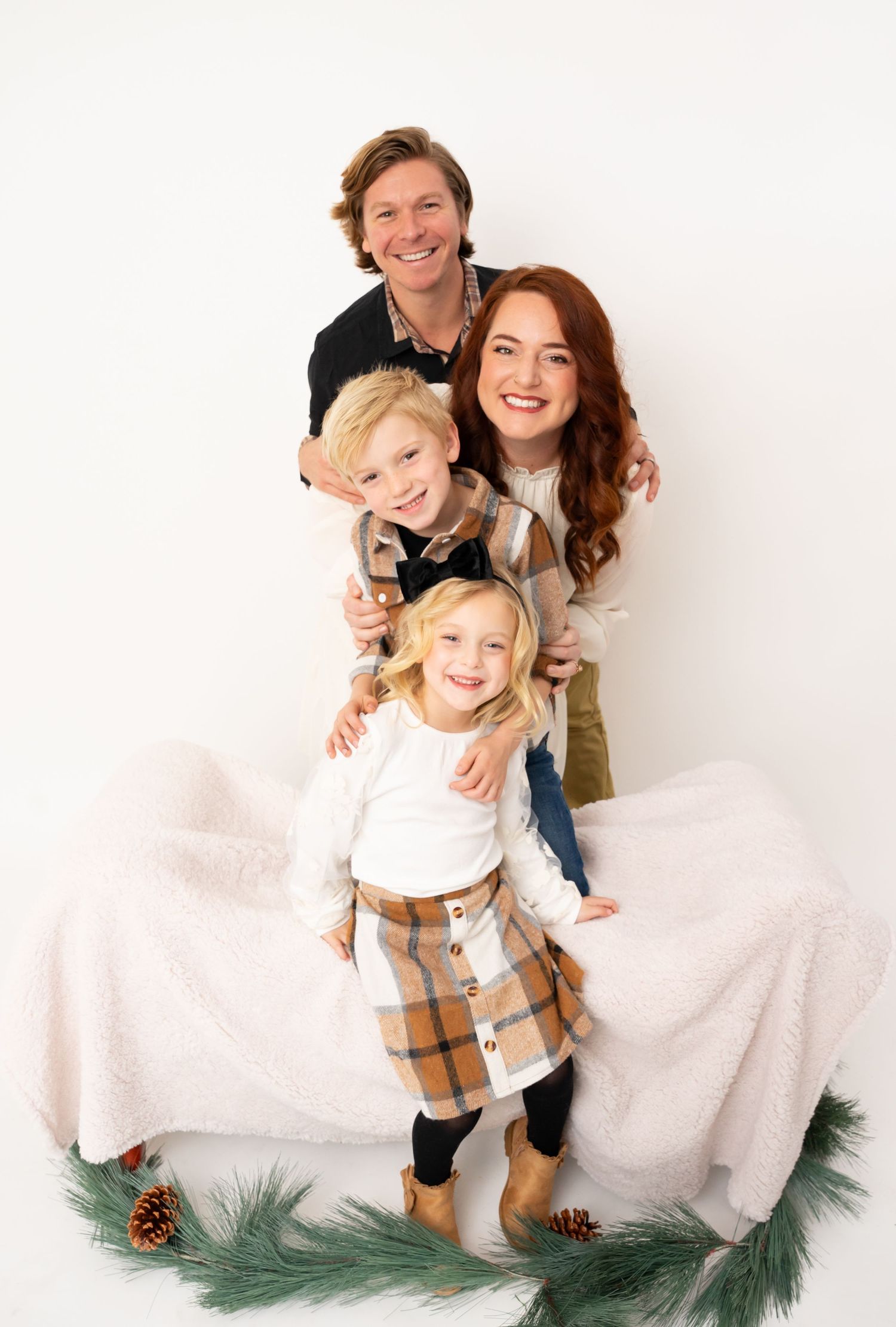 A family group posing together with holiday greenery and pinecones against a white backdrop.