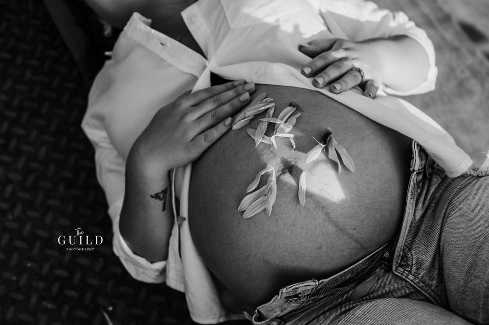 Black and white close-up of a pregnant belly with delicate white flowers resting on it during a maternity shoot.