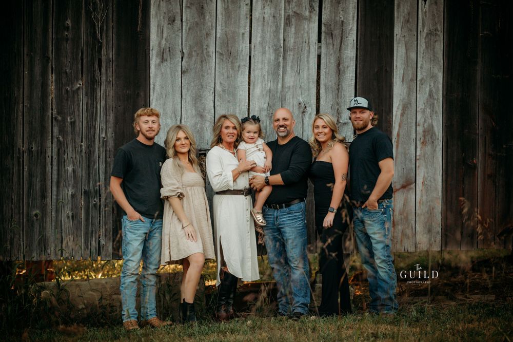 Family of seven posing in front of a rustic barn for a professional outdoor portrait session.