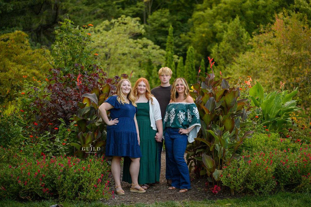 Mother with three children posing among vibrant colorful garden foliage for family portrait session.