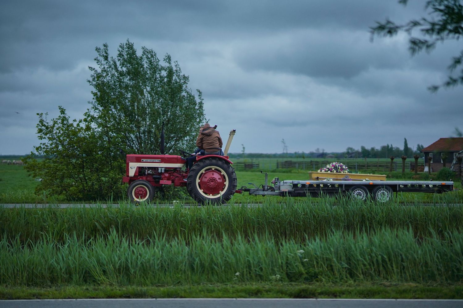 Red vintage tractor working in a lush green agricultural field under stormy skies.