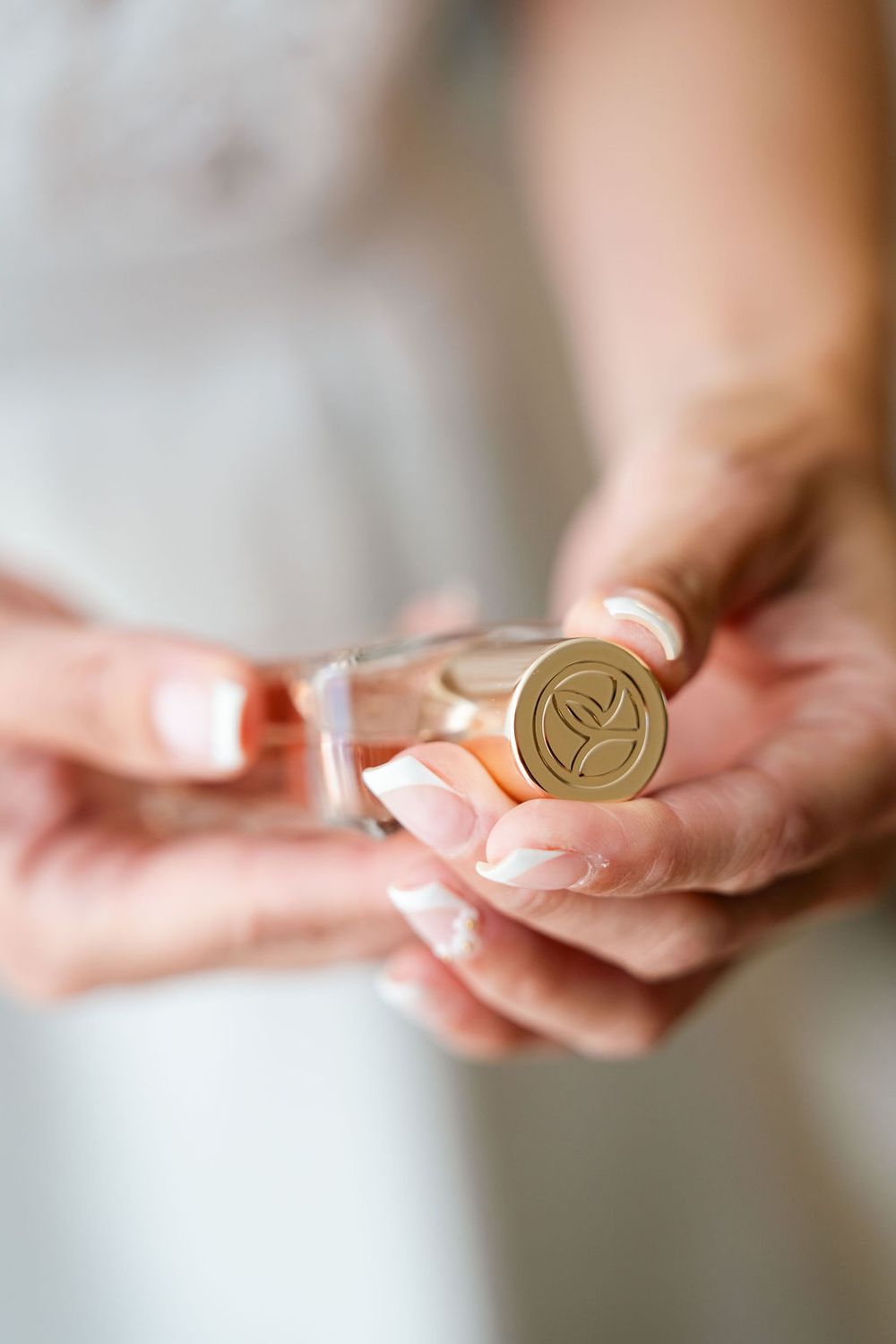 Bride holding a gold Natura perfume bottle cap with French manicured nails on her wedding day.
