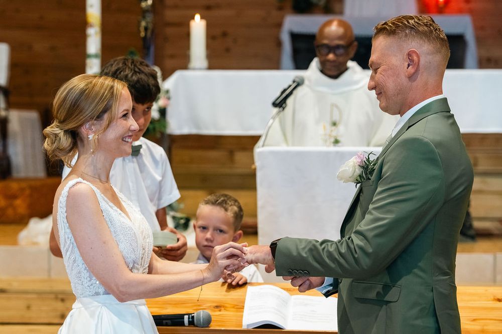 Bride and groom exchange rings at church altar during wedding ceremony with officiant in background.