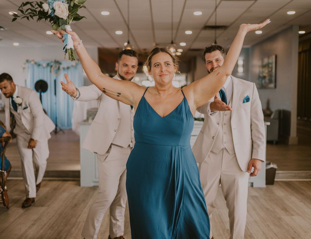 Bridesmaid in teal dress celebrates with groomsmen in white suits at a wedding reception venue.