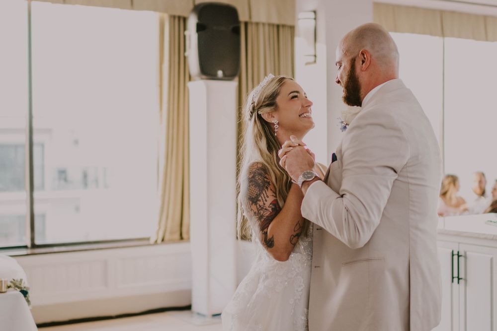 A bride and groom share their first dance, smiling joyfully in a bright, elegant wedding venue.