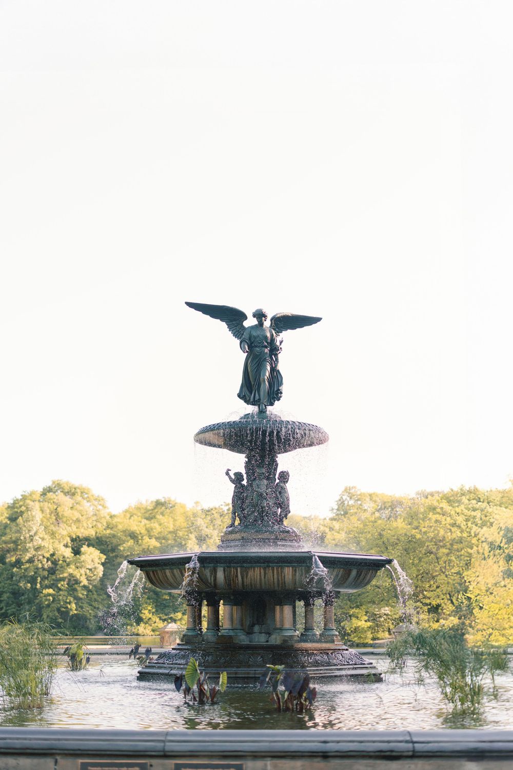 Bethesda Fountain in Central Park featuring an angel statue atop a tiered bronze fountain surrounded by lush trees.