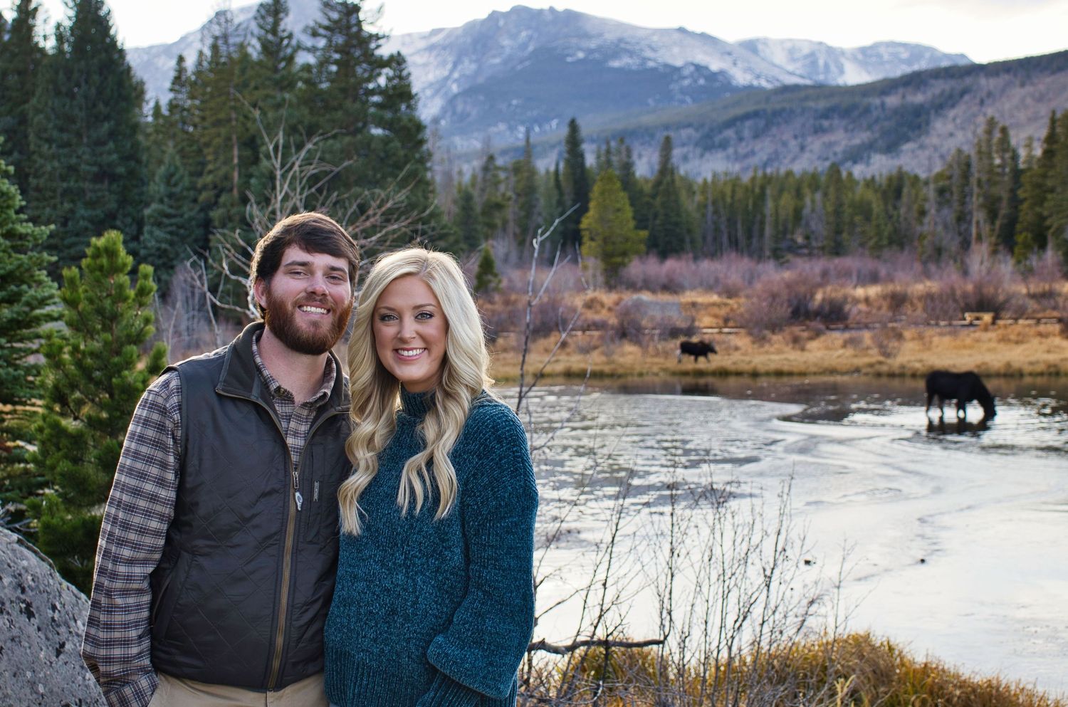 Couple posing after his proposal to her with moose and mountains in the background.